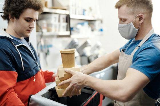 A dark-haired young man holds a cooler while another young man places food in to-go containers inside it